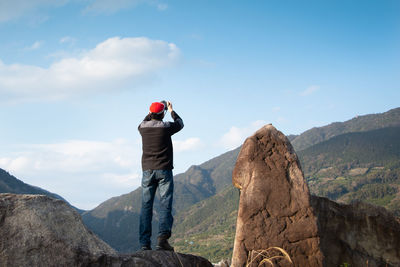 Man on rock by mountains against sky