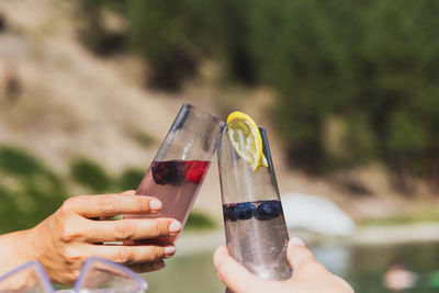 Two glasses touching for a cheers near an outdoor natural pool or hot spring.