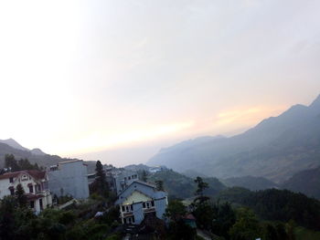 Scenic view of buildings and mountains against sky during sunset