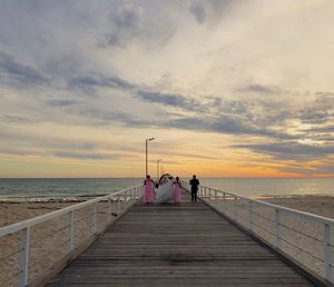 People on pier over sea against sky during sunset