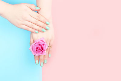 Female hands with trendy manicure neo-mint on a pink and blue background with copy space, a top view