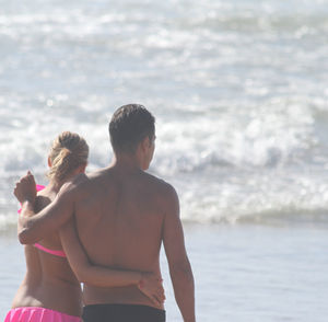 Rear view of couple walking at beach during sunny day