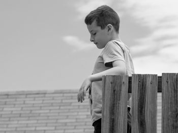 Boy standing by wooden posts at footpath against sky