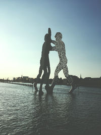 Silhouette people on riverbank against clear sky