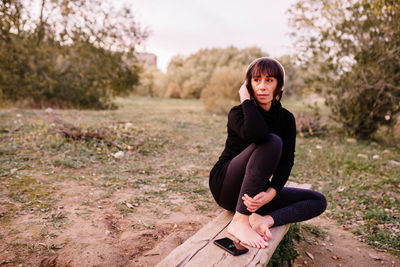 Full length of woman sitting on wooden bench at park