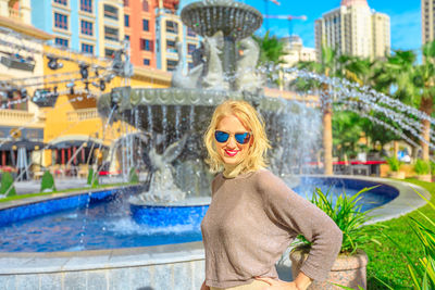 Portrait of smiling woman in sunglasses standing against fountain