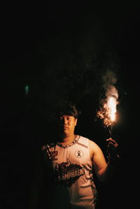 Portrait of young man standing against dark sky