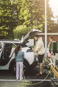 Father talking to daughter charging electric car at station