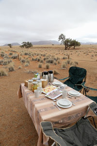 Table and chairs on field against sky