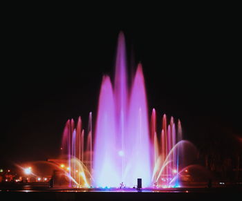 Illuminated fountain in city against sky at night