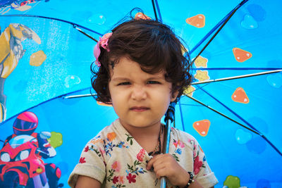 Portrait of cute girl making face while holding blue umbrella