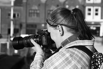 Woman photographing against buildings in city