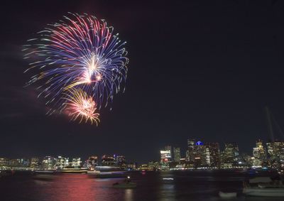 Firework display over illuminated city against sky at night