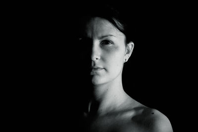 Close-up portrait of shirtless young woman standing against black background