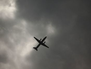 Low angle view of airplane flying against cloudy sky