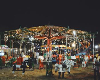 Illuminated carousel in amusement park against clear sky at night