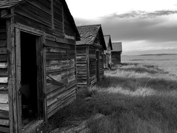 Abandoned wooden houses on grassy field against sky