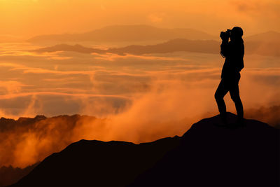 Silhouette man photographing against sky during sunset