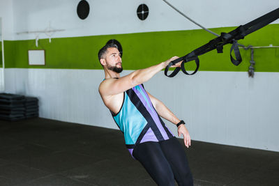 Side view of young muscular man in sportswear training with elastic resistance bands during intense workout with friend in modern gym