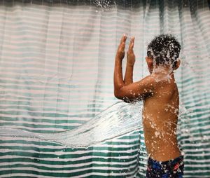 Water splashing on shirtless boy against curtain
