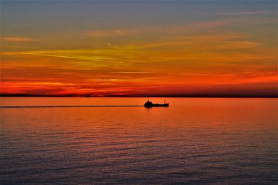 Silhouette boat in sea against orange sky