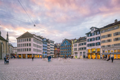 People walking on street amidst buildings in city against sky