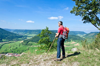 Side view of backpack man standing on mountain against sky