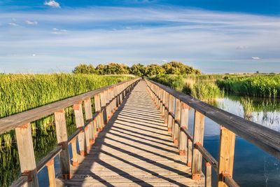 View of wooden footbridge over sea against sky