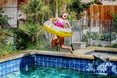 Full length of happy girl with inflatable ring jumping into swimming pool