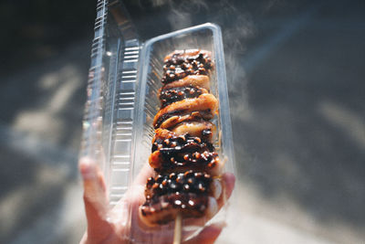 Close-up of hand holding meat on barbecue grill
