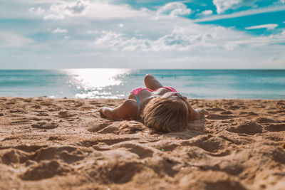 Rear view of man sitting on shore at beach against sky