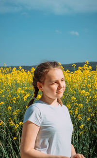 Cropped hand of woman standing amidst yellow flowering plants on field against sky