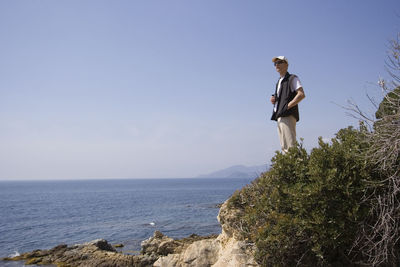 Man standing on mountain by sea against clear sky