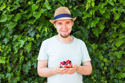 Portrait of smiling young man holding fruit while standing against plants