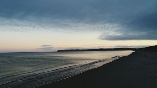 Scenic view of beach against sky at sunset