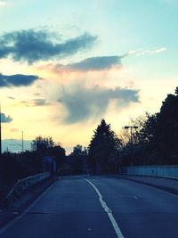 Road by silhouette trees against sky at sunset