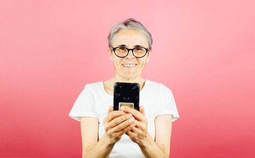 Young woman using mobile phone against pink background