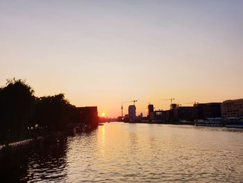 River by silhouette buildings against sky during sunset