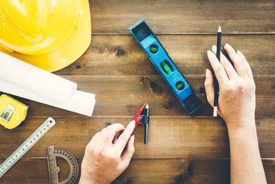 Cropped hands of architect holding pencils by work tools on table