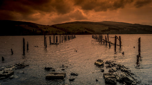 Wooden posts on beach against sky during sunset