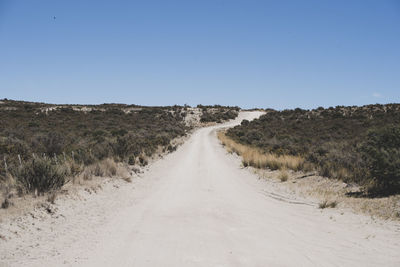 Dirt road amidst land against clear sky