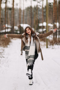 A funny pretty curly-haired girl in winter clothes is having fun walking alone in a snowy forest