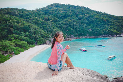 Full length portrait of woman sitting on rock against sea