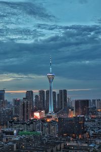 Illuminated buildings in city against cloudy sky