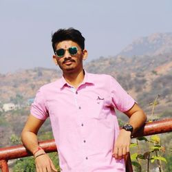 Portrait of young man wearing sunglasses standing against sky