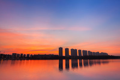 Scenic view of lake and buildings against sky during sunset