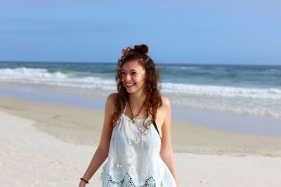 Portrait of young woman standing on beach against sky