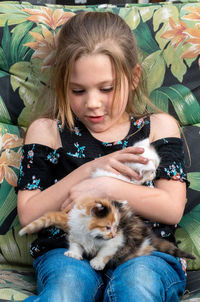 Little girl struggles to hold on to two new kittens, as they climb all over her lap