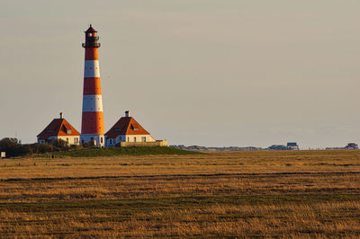 Lighthouse on field by building against sky