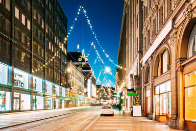 Illuminated street amidst buildings in city at dusk